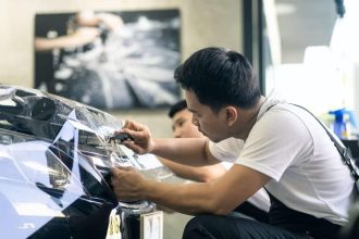 Technicien appliquant un film de protection sur une voiture noire dans un garage